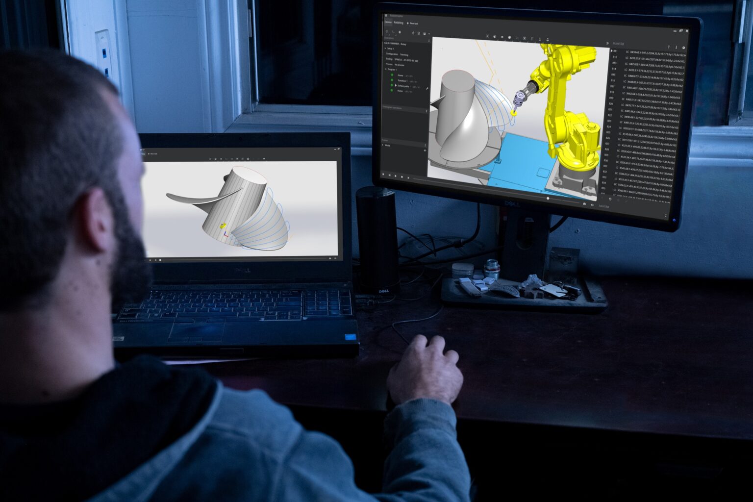 An engineer using offline CAD/CAM software on a computer to program and simulate a robotic machining process.