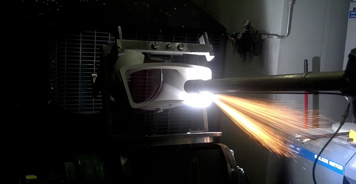 An industrial robot is performing a thermal spraying operation on a workpiece, guided by a program created with Robotmaster offline programming software.